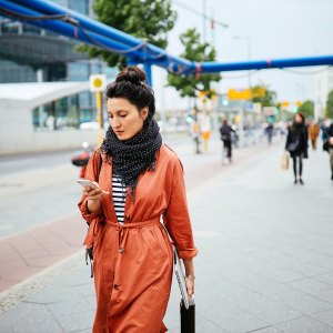 Young commuter woman, walking in Berlin, carrying her laptop, checking apps on the mobile phone.