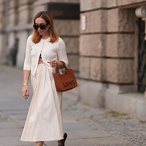 BERLIN, GERMANY - AUGUST 22: Sonia Lyson seen wearing Loewe brown sunglasses, Zara creamy white cotton buttoned cardigan, matching Zara creamy white long pleated skirt, Loewe cognac brown logo raffia bag and Zara burgundy leather ballerinas, on August 22, 2024 in Berlin, Germany. (Photo by Jeremy Moeller/Getty Images)
