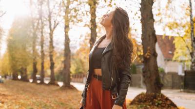Woman standing in autumn park, breathing deeply and smiling with closed eyes