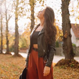 Woman standing in autumn park, breathing deeply and smiling with closed eyes