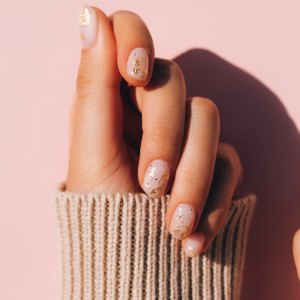 Glowing hands in sweater with knitted sleeves and with nude color manicure with gold particles on pink table. Trendy colors of the year