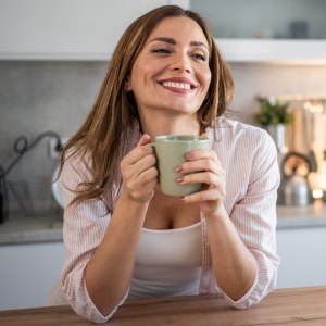 A young woman enjoys her kitchen, dressed in pajamas, drinking her morning coffee