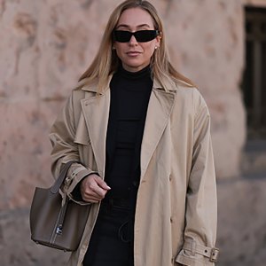 BERLIN, GERMANY - OCTOBER 08: Sonia Lyson is seen wearing black rectangular sunglasses featuring wide temples with triangular logo embellishment from Prada; several earrings and ear studs in silver and gold; an outfit from Levi's consisting of a calf-length beige trench coat with notch lapels and belted cuffs, a black fitted turtleneck, and dark grey wide-legged jeans with a tie belt; and a rectangular brown leather "Picotin" handbag with white decorative seams from Hermès on October 08, 2024, in Berlin, Germany. (Photo by Jeremy Moeller/Getty Images)