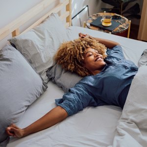 Woman is lying in her bed in the morning. She is stretching and smiling.