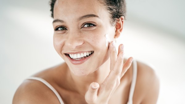 Smiling young women applying moisturiser to her face