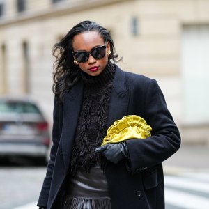 PARIS, FRANCE - OCTOBER 18: Emilie Joseph wears oversized double breasted wool extra long coat from COS, chocolate wool blended fringed turtleneck jumper from COS, lack leather long gloves, Black sunglasses from Gentle Monster, a satin yellow clutch/pouch bag, during a street style fashion photo session, on October 18, 2024 in Paris, France. (Photo by Edward Berthelot/Getty Images)