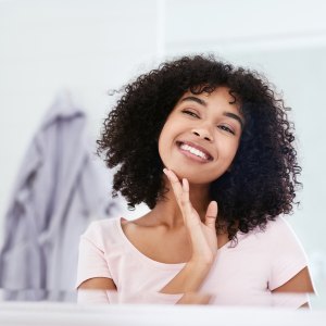 Cropped shot of an attractive young woman smiling while admiring her face in the bathroom mirror at home