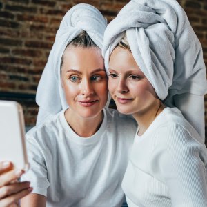 A smiling Caucasian female and her pretty daughter looking themselves in the mirror after taking a shower.