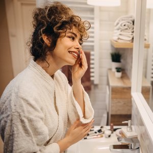 Beautiful young woman in a bathrobe looks in the mirror in her bathroom
