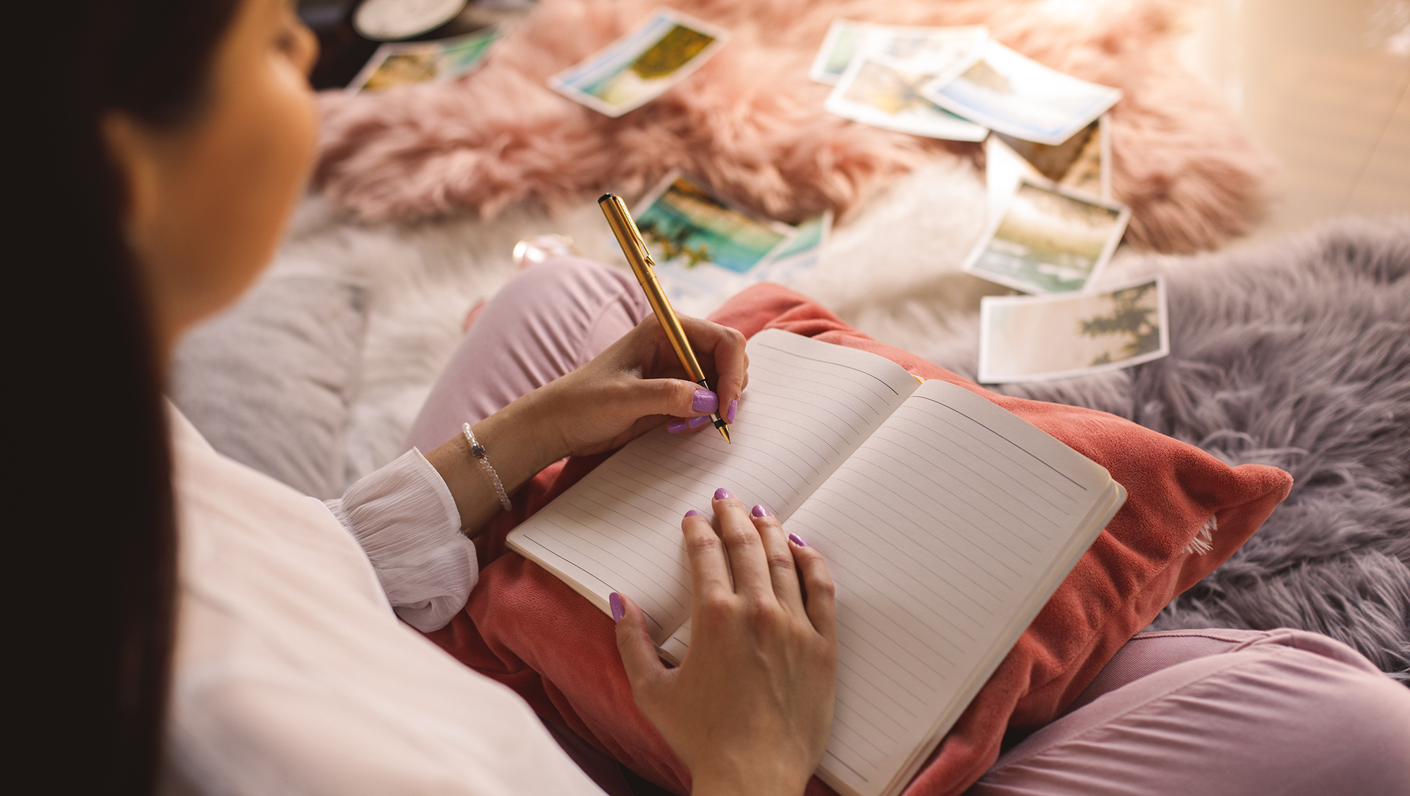High angle view of young woman sitting comfortably on bedroom floor and writing memories in her diary.