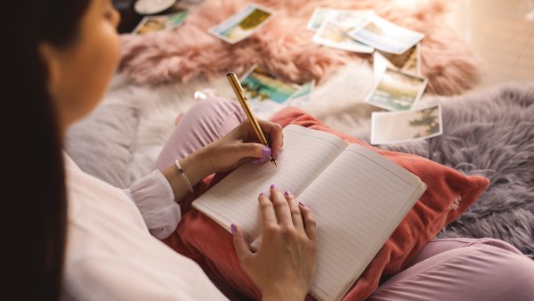 High angle view of young woman sitting comfortably on bedroom floor and writing memories in her diary.