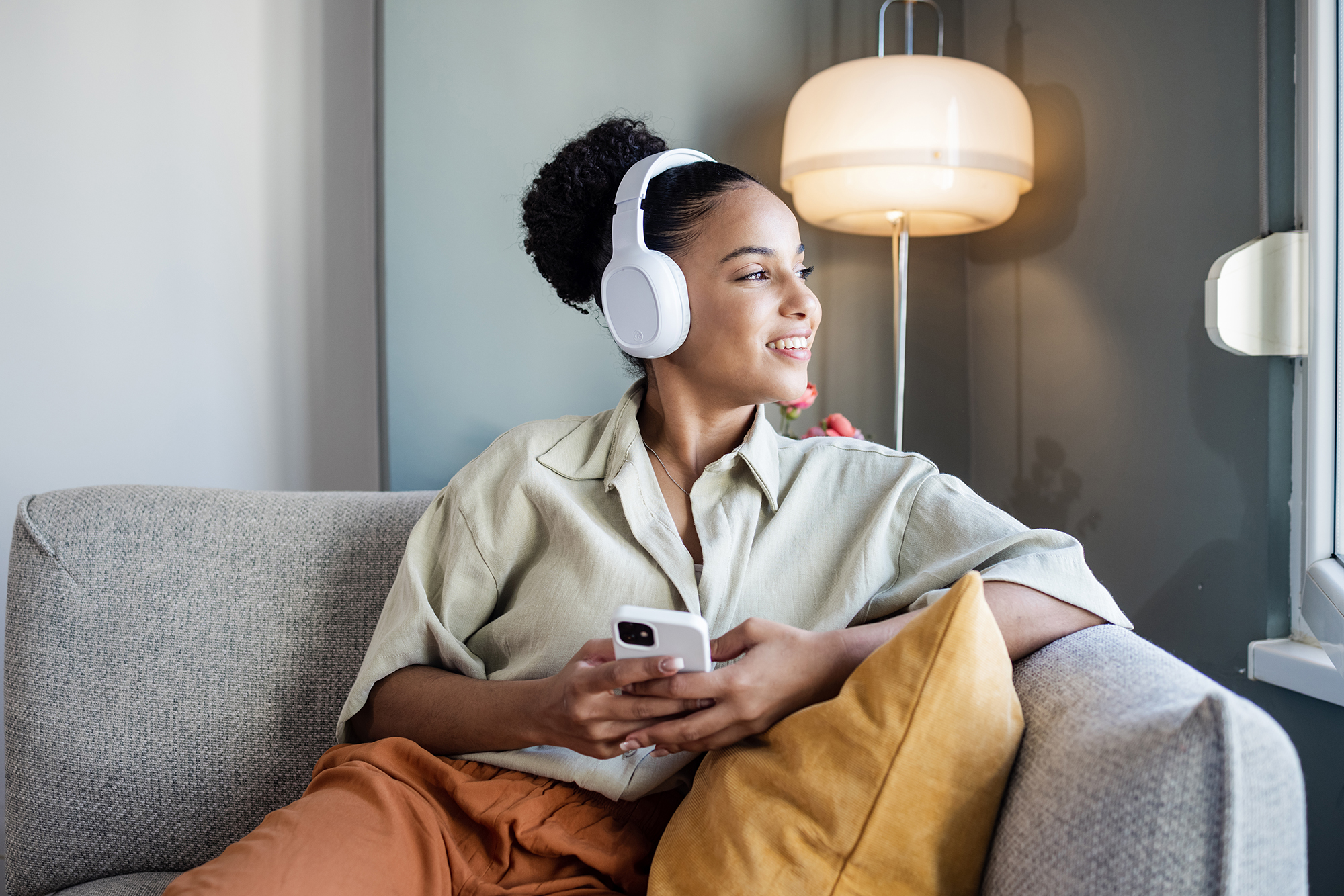Young African American woman with wireless headphones relaxing on the couch and listening her favourite music on smart phone