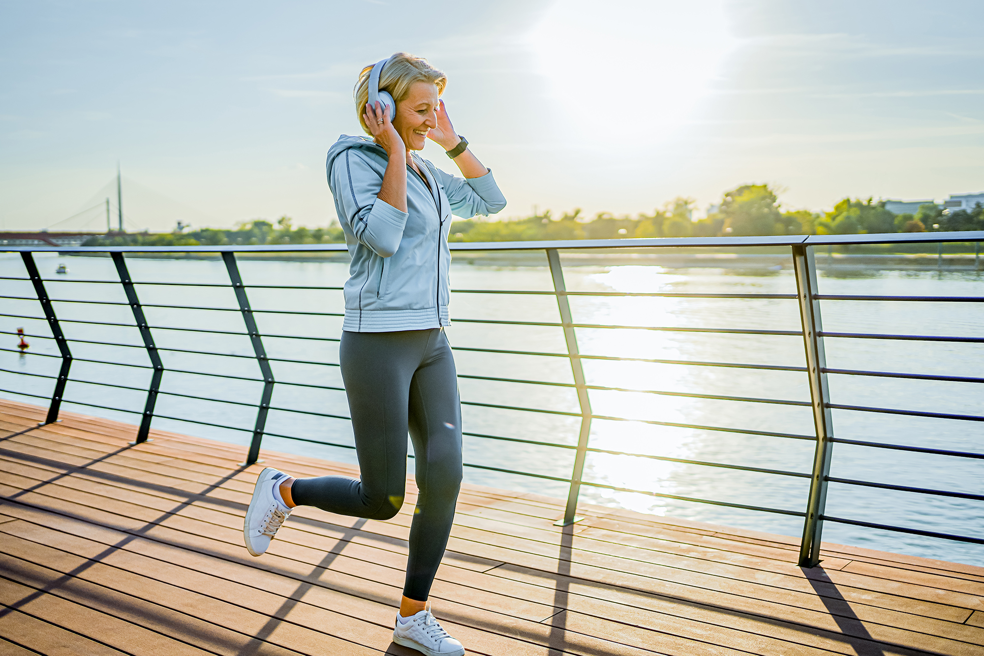 Cheerful mature woman with headphones jogging on the riverside
