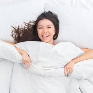 Young brunette woman on bed top view looking camera laughing cheerful