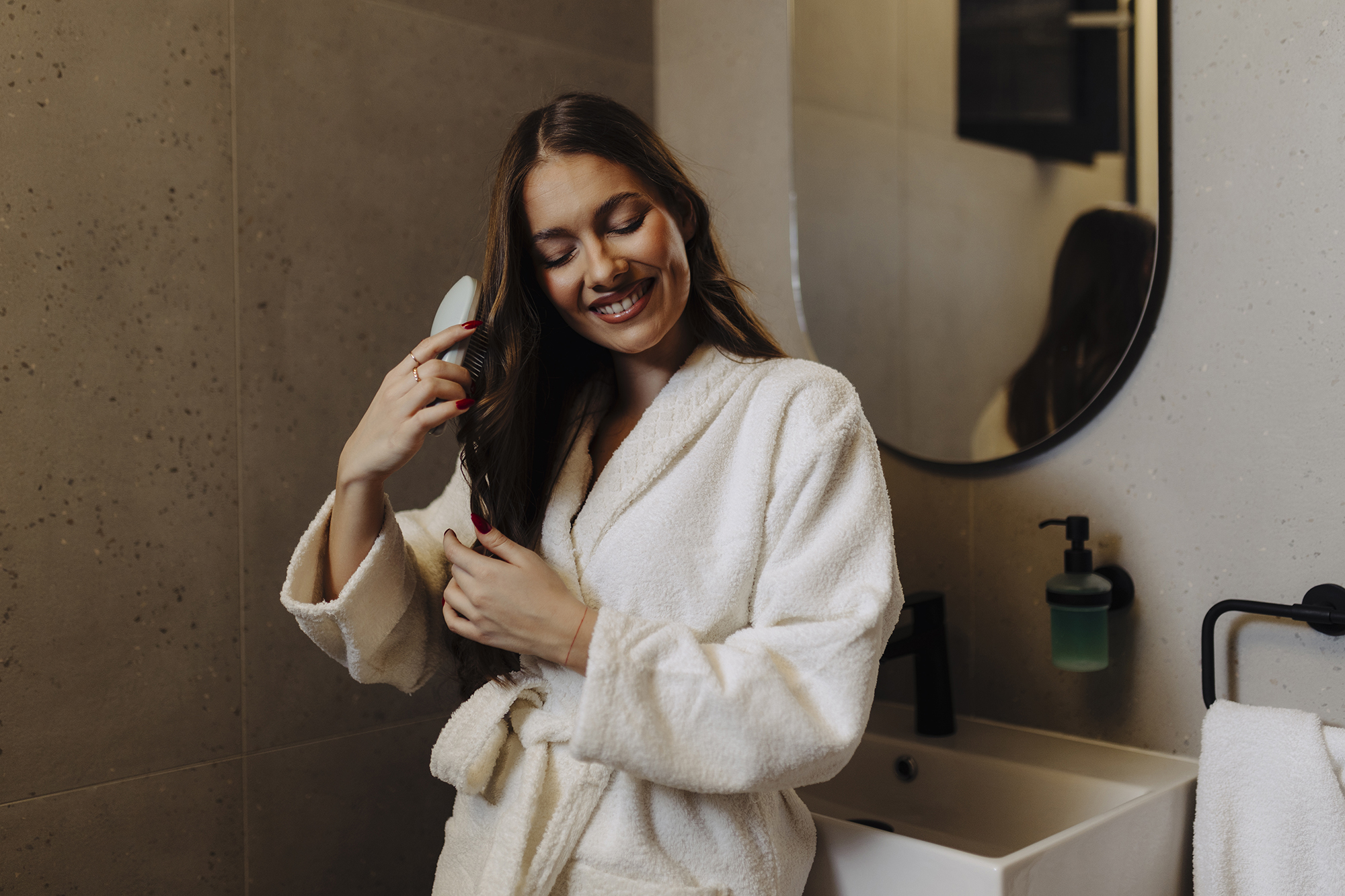 Woman Combing Her Beautiful Hair With Brush While Standing Near Mirror In Bathroom