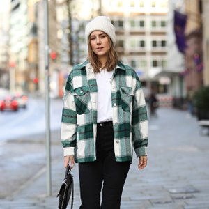 woman wearing green plaid shacket, black pants and white beanie
