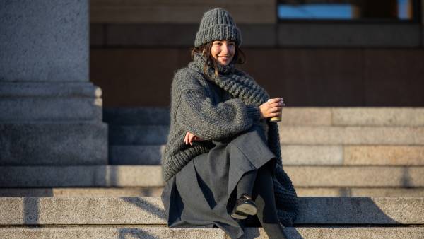 COPENHAGEN, DENMARK - FEBRUARY 01: Benthe Liem sitting drinking coffee wears grey beanie, knit, scarf, skirt, black Prada bag outside Marimekko during the Copenhagen Fashion Week AW24 on February 01, 2024 in Copenhagen, Denmark. (Photo by Christian Vierig/Getty Images)