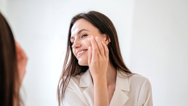 Healthy skin and everyday skincare routine concepts. Portrait of happy female apply anti aging moisturizing cosmetic cream on face, smiling, looking at bathroom mirror