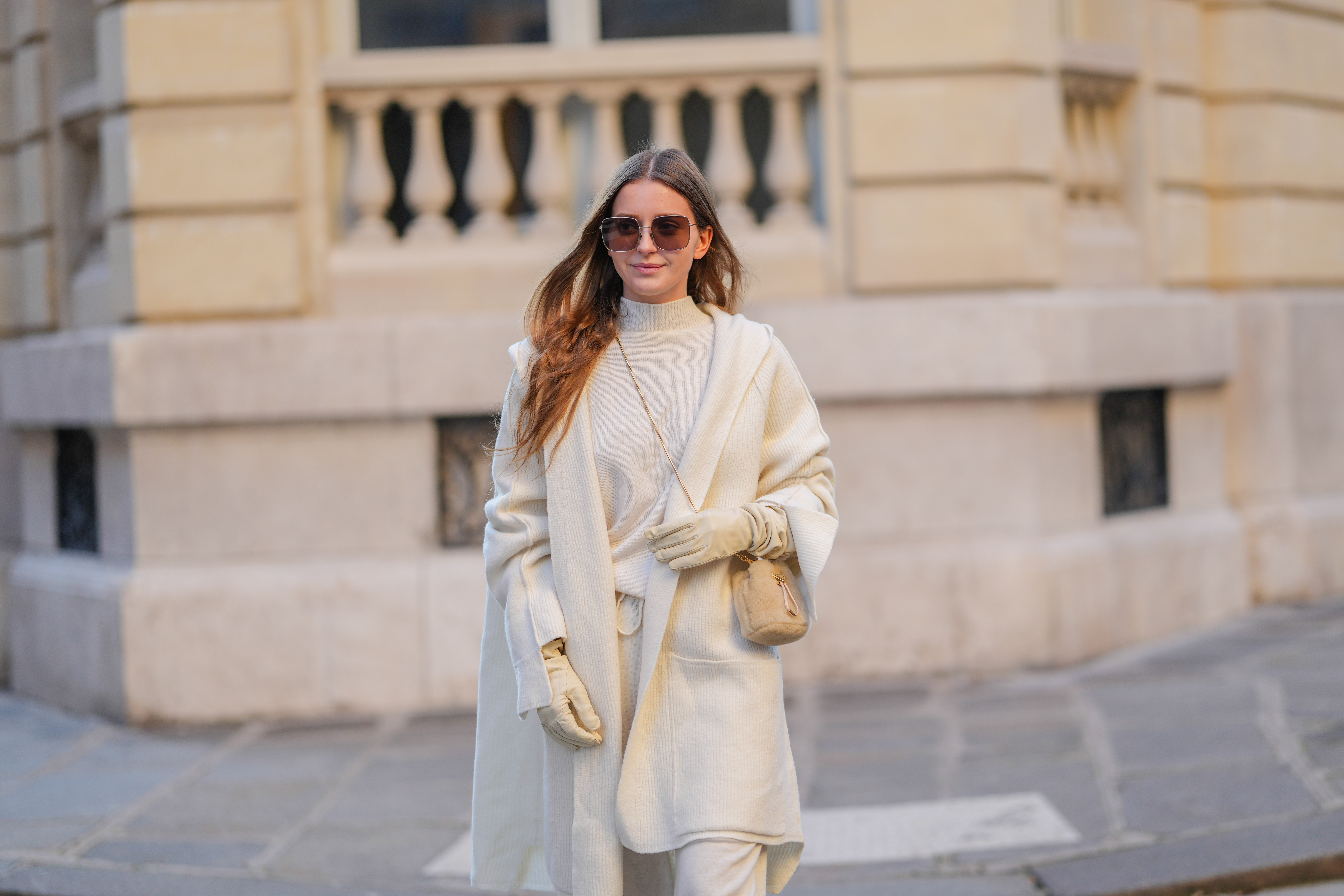 Diane Batoukina wears brown Dior sunglasses, a white cashmere Zara turtleneck pullover, matching coat and pants, a light brown fluffy faux fur Prada bag, white leather gloves, during a street style fashion photo session, on January 13, 2025 in Paris, France.