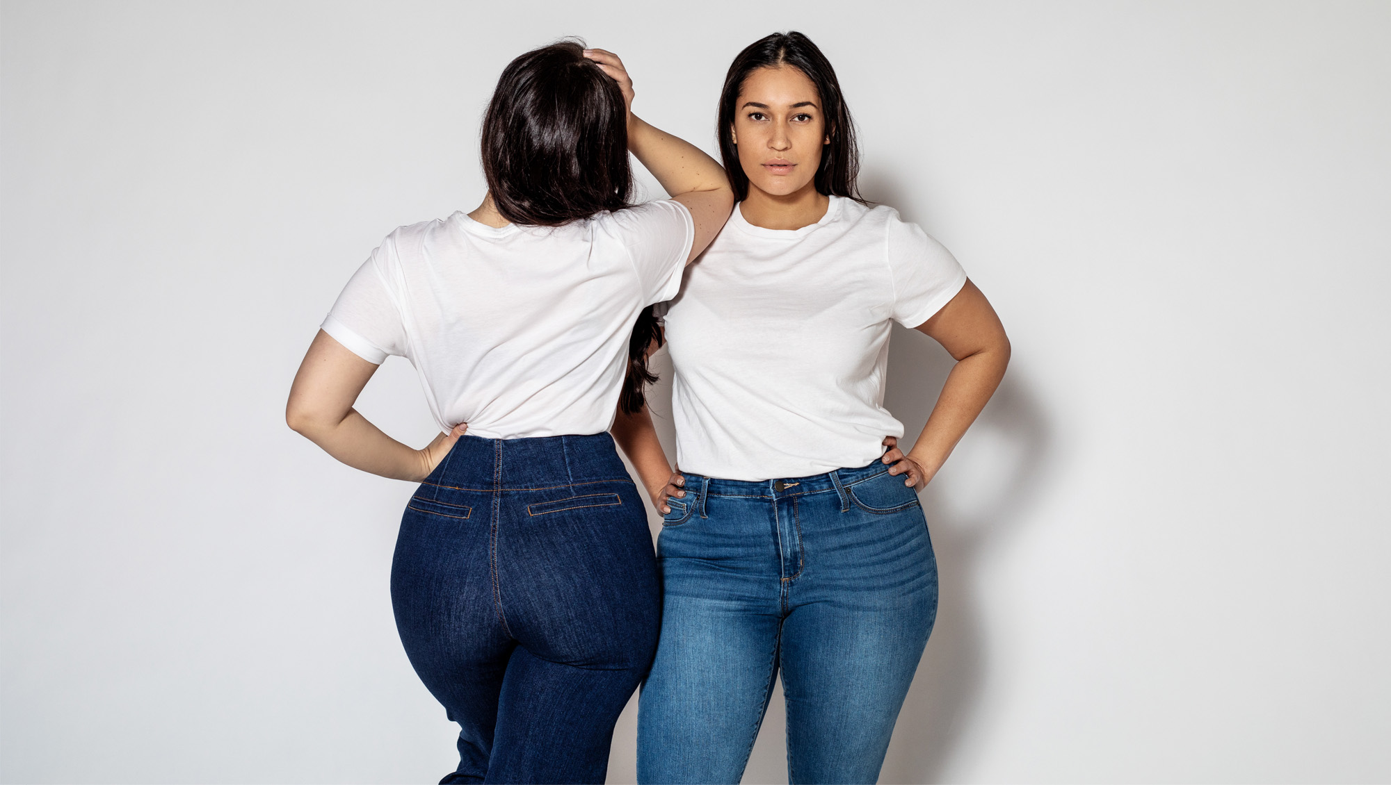 Portrait of two plus size female standing in opposite directions on white background. Women wearing white t-shirt and blue denim jeans.