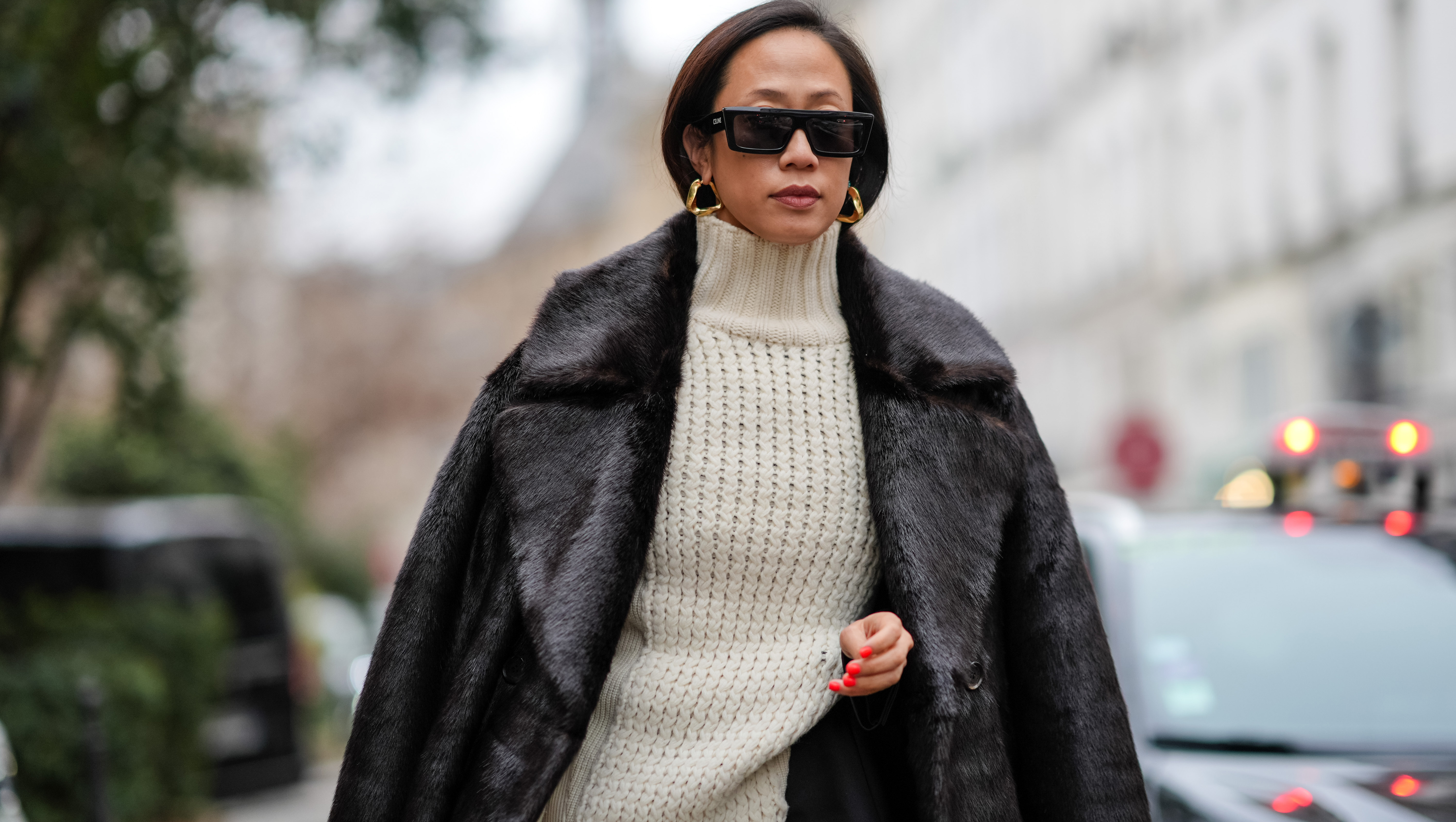 PARIS, FRANCE - JANUARY 21: A guest wears sunglasses, earrings, a white ribbed wool long pullover worn as a dress, a black fluffy long coat, outside Sacai, during the Menswear Fall/Winter 2024/2025 as part of Paris Fashion Week on January 21, 2024 in Paris, France. (Photo by Edward Berthelot/Getty Images)