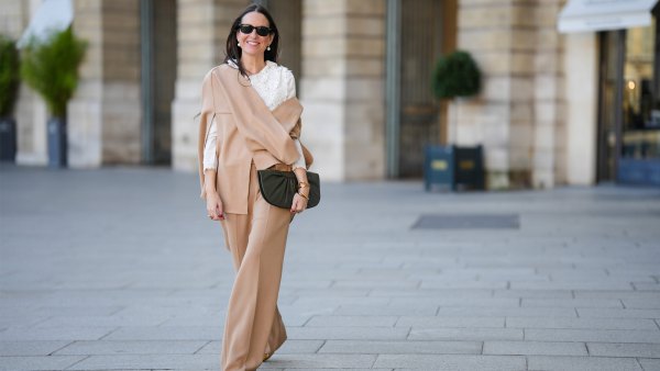 Alba Garavito Torre wears black sunglasses from Ray Ban, white large pearls earrings, a white shirt with cut-out lace pattern large collar, a beige felt / wool oversized cloak, matching beige wool / felt palazzo pants, a black shiny leather ruffled handbag, a gold Love bracelet from Cartier, gold bracelet, gold rings, brown leather pointed pumps heels shoes, during a street style fashion photo session, on October 28, 2021 in Paris, France.