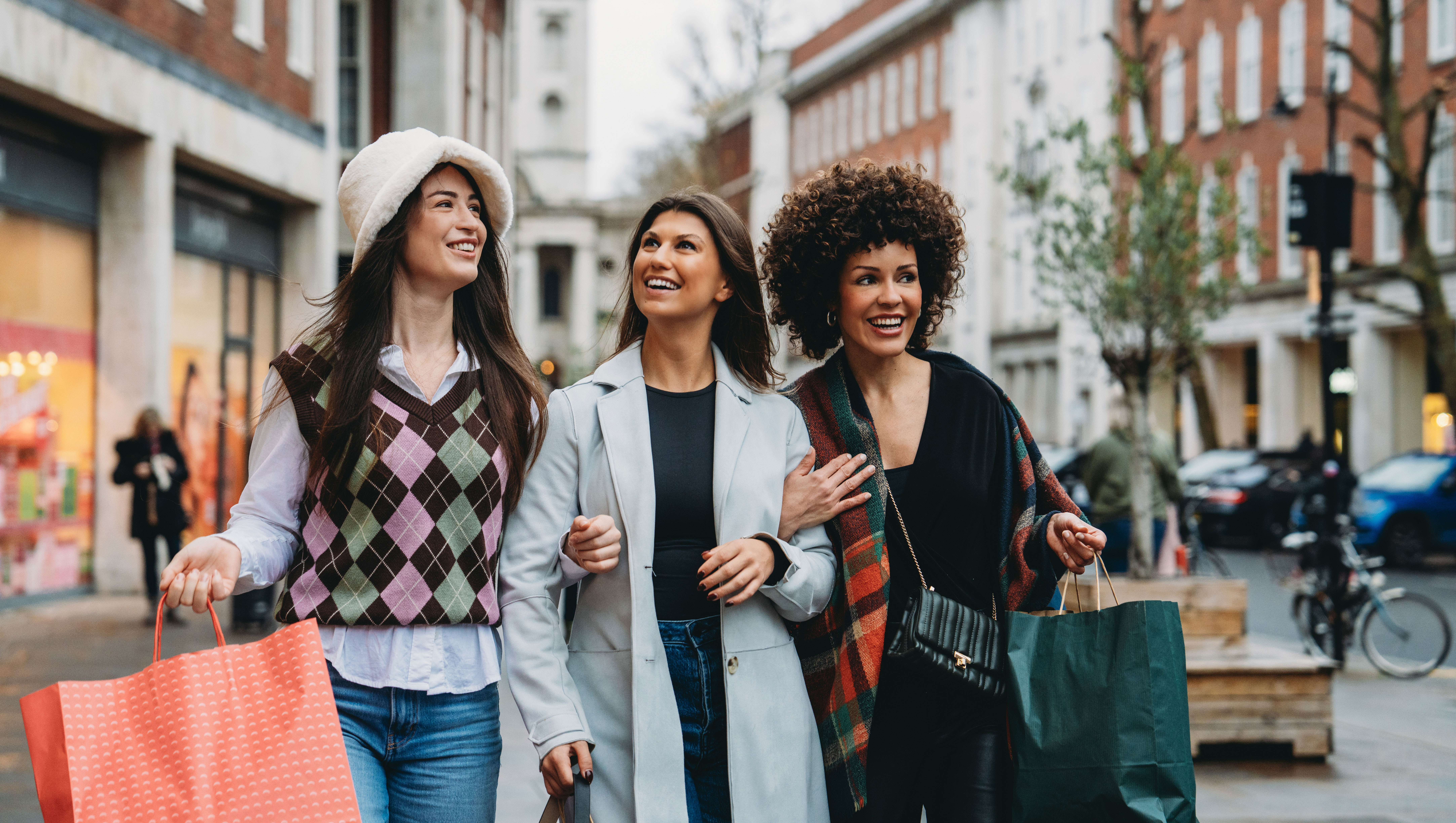 Three cheerful female friends enjoy a shopping spree, carrying bags and strolling down a bustling city street