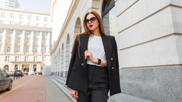 Beautiful urban fashion woman in a stylish black casual suit with vintage sunglasses walks in the city. Pretty business lady
