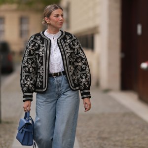 BERLIN, GERMANY - APRIL 08: Aline Kaplan seen wearing gold heart shaped earrings, Sézane black / white flower embroidered jacket, Mango white cotton blouse, Citizen Of Humanity blue denim wide leg jeans, Le Tanneur blue leather bag, on April 08, 2024 in Berlin, Germany.