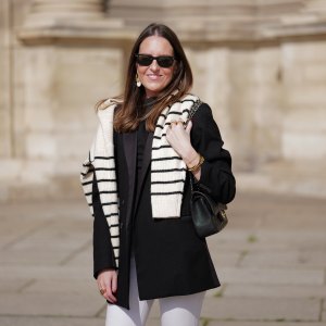 woman wearing black coat, striped sweater and white pants