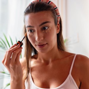 Portrait of a young girl looking at herself in the mirror while applying concealer on her face