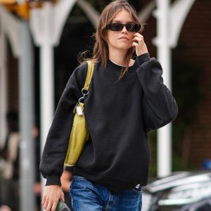 NEW YORK, NEW YORK - SEPTEMBER 07: A model wears black sunglasses, black oversized sweater, light yellow green leather bag, washed dark blue denim jean pants, black sneaker shoes , outside Tibi, during the New York Fashion week Spring/Summer 2025 on September 07, 2024 in New York, New York. (Photo by Edward Berthelot/Getty Images)
