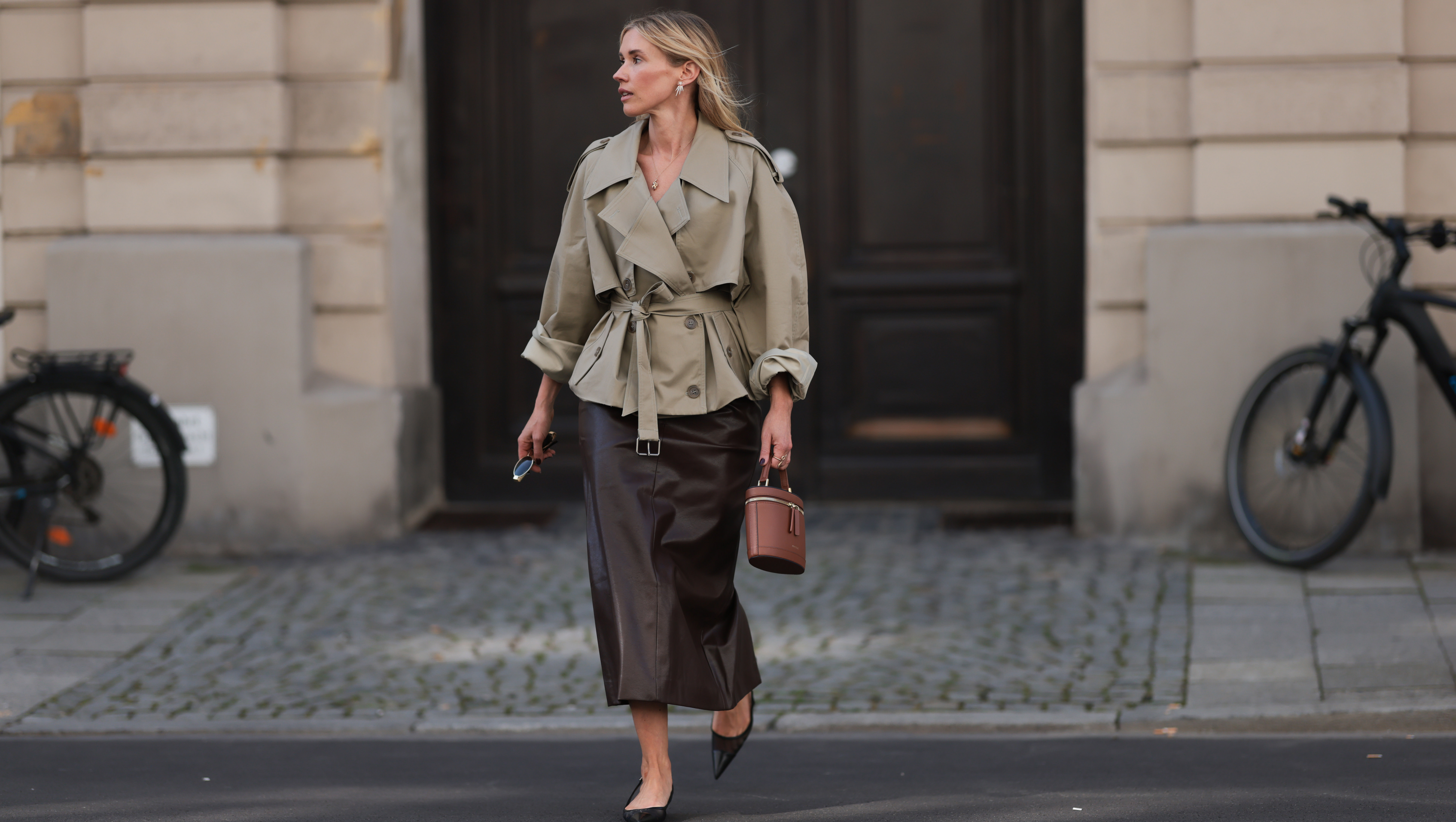 MUNICH, GERMANY - SEPTEMBER 22: Jennifer Zimmermann is seen wearing gold and diamond shooting star-shaped earrings from Ole Lynggaard; a fine yellow gold necklace with a yellow gold elephant pendant, also from Ole Lynggaard; an outfit from Pixie Market, consisting of a beige oversized cropped trench coat with tied belt and oversized lapel, and a brown leather midi pencil skirt; a brown leather oval-shaped handbag from PARIS/64 with a gold zipper; a gold snake ring; holding oval sunglasses with a fine gold frame and wide temples from Celine; and pointed black leather slingback kitten heels from Saint Laurent, on September 22, 2024 in Munich, Germany. (Photo by Jeremy Moeller/Getty Images)