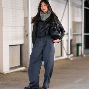 NEW YORK, NEW YORK - FEBRUARY 07: A guest wears dark gray scarf, shiny black cropped leather jacket, shiny black leather bag, dark gray pinstripe high waisted loose trouser pants, shiny black pointed toe heeled boots leather shoes, outside Theory, during the New York Fashion week Fall/Winter 2025 on February 7, 2025 in New York, New York. (Photo by Edward Berthelot/Getty Images)