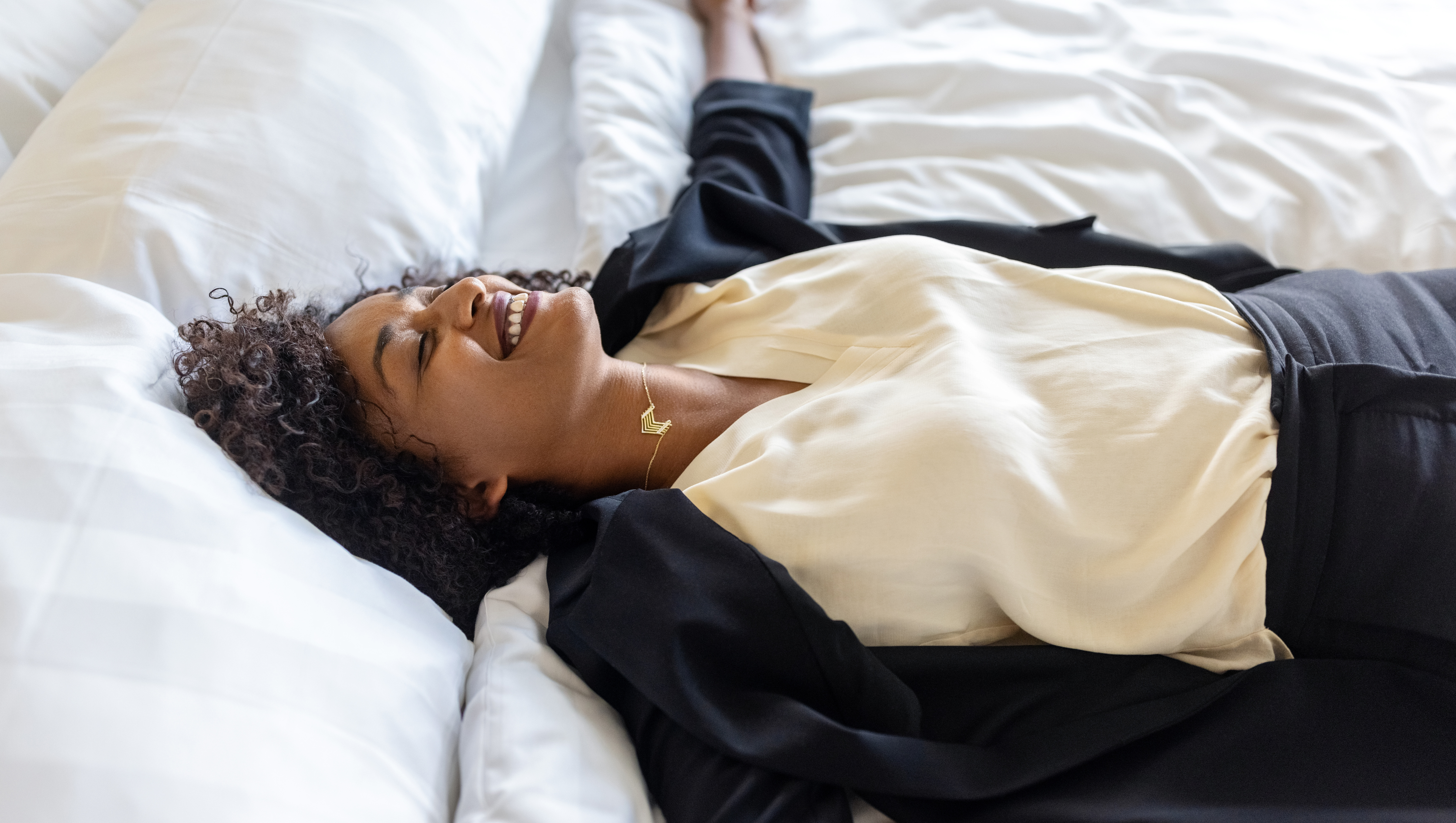 Tired mid adult businesswoman lying on hotel bed after her trip. Tired woman in formal clothes resting on hotel bed with her arms outstretched and smiling.