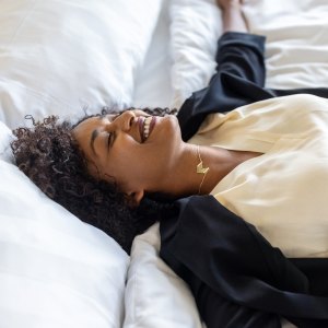Tired mid adult businesswoman lying on hotel bed after her trip. Tired woman in formal clothes resting on hotel bed with her arms outstretched and smiling.