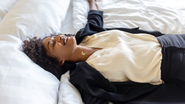Tired mid adult businesswoman lying on hotel bed after her trip. Tired woman in formal clothes resting on hotel bed with her arms outstretched and smiling.