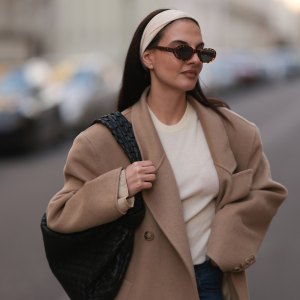 BERLIN, GERMANY - FEBRUARY 25: Anna Winter seen wearing brown tortoise oval sunglasses, Raey creamy white basic shirt, matching creamy white hair band, Source Unknown beige overside wool long coat, Rotate dark blue skinny jeans / denim pants, Bottega Veneta black leather woven Jodie bag, on February 25, 2024 in Berlin, Germany.