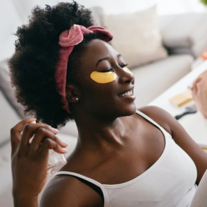 Beautiful young woman with under eye patches, sitting and enjoying the scent of a beautiful perfume.