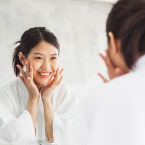 Asian woman cleaning face front of mirror, skin care and cosmetic removal concept