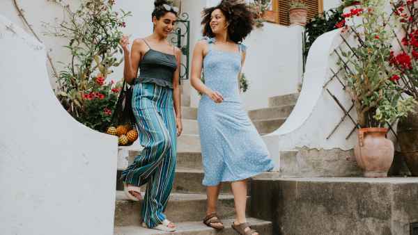 Two beautiful young woman descend a set of concrete steps from European-style apartments as they have a conversation.