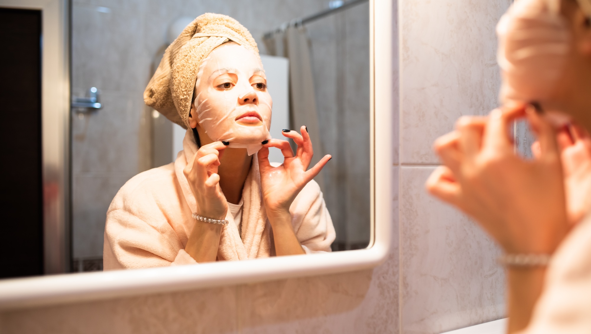 Woman applying a sheet mask in the bathroom mirror
