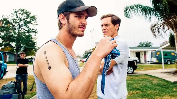 A man drinks water while another man stands behind him in 99 Homes.