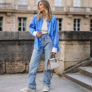PARIS, FRANCE - MAY 10: Xenia Adonts wears a blue oversized long shirt with white collar and white cuffs from Attire The Studio, a white ribbed asymmetric top from Attire The Studio, blue denim jeans wide-leg pants from Anine Bing, a beige Kelly Hermes bag, sneakers from Converse x Kim Jones, on May 10, 2021 in Paris, France. (Photo by Edward Berthelot/Getty Images)