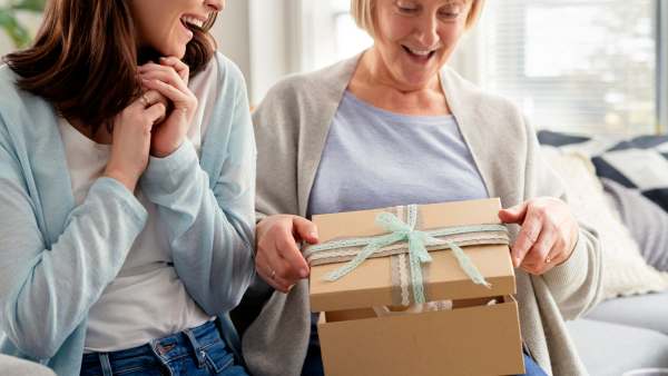 Excited adult daughter waiting for mom to open the gift