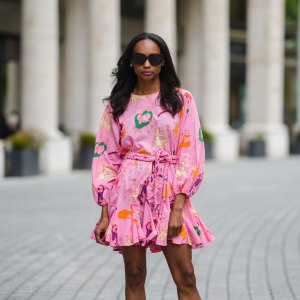 Emilie Joseph @in_fashionwetrust wears sunglasses, silver earrings, a Rhode printed summer vacay Ella dress in vibrant pink with long dolman sleeves with elastic cuffs and a full a flirty hem and a waist-cinching braided belt, on May 27, 2021 in Paris, France.