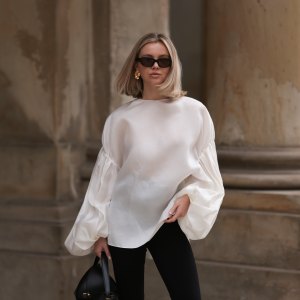 Isabelle Hartmann seen wearing Vehla Eyewear black / brown sunglasses, Nootka gold earrings, Khaite oversized puffy ruffled long sleeve silk top, Isabelle Hartmann x Edited black slit pants and Toteme black leather bag on April 05, 2024 in Hamburg, Germany.