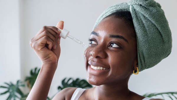 Happy young woman applying face serum at home - stock photo
