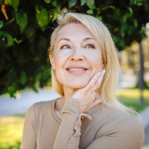Natural beauty care: Beautiful blonde woman poses near a green tree in summer, emphasizing her natural approach to body and skincare - stock photo