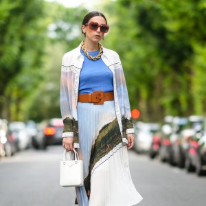 PARIS, FRANCE - AUGUST 02: Gabriella Berdugo wears Loewe sunglasses, a golden large maxi chain necklace, a blue top, a long shirt with colored printed landscape details from Icicle, a matching pleated midi skirt with printed landscape details from Icicle, a white Prada bag, a leather brown large belt from Barbara Bui, green square sandals from Reike Nen, on August 02, 2021 in Paris, France. (Photo by Edward Berthelot/Getty Images)